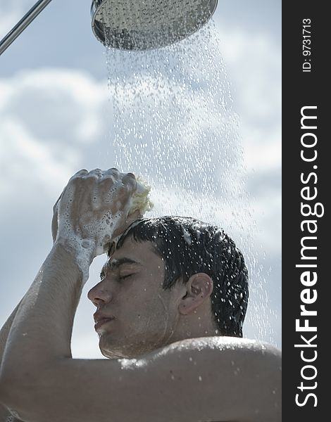 Handsome young topless caucasian man taking an outdoor shower on beach